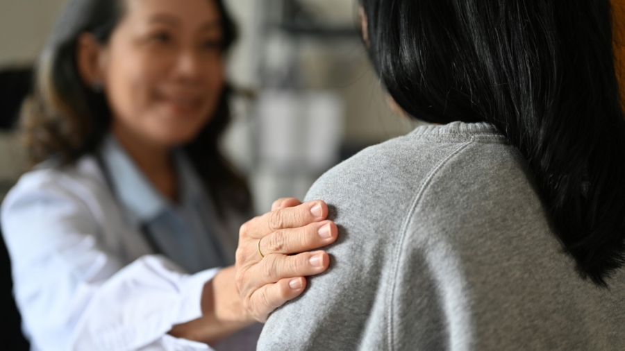 An aged Asian female doctor touching shoulder to comfort and support her patient. A young Asian female patient is being reassured by her doctor. close-up image